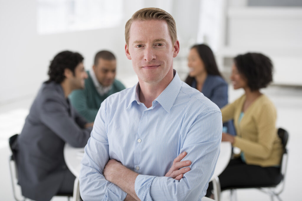 smiling man with arms crossed stands in front of meeting