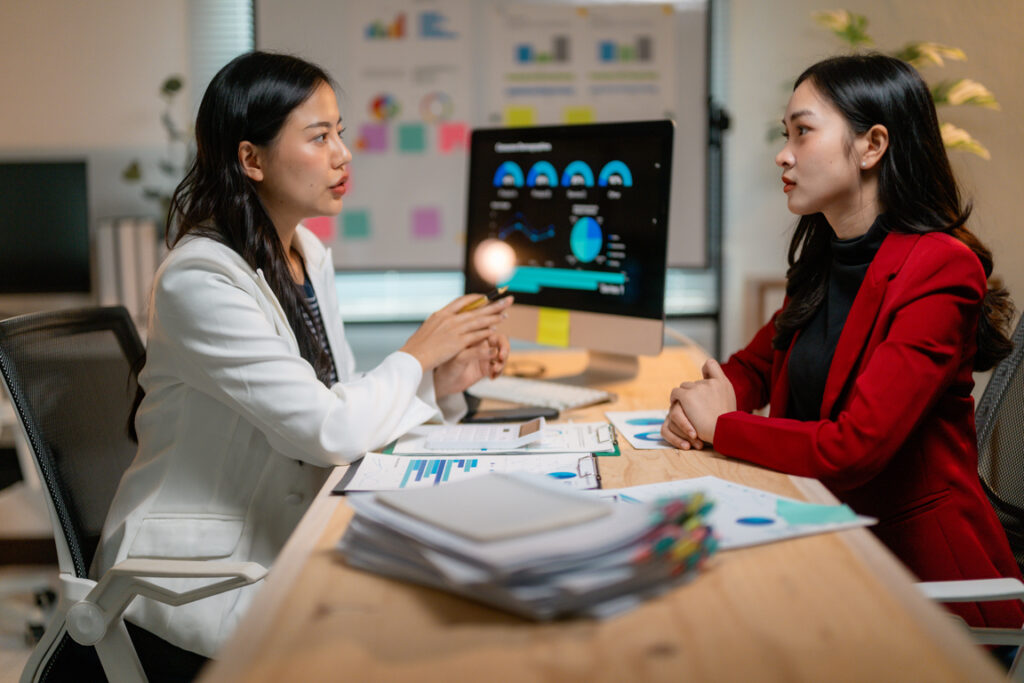 Two asian businesswomen discussing marketing strategy showing financial graphs on computer screen in the office