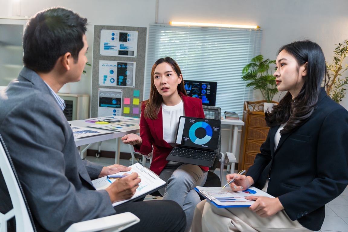 Asian businesspeople discussing and analyzing financial charts and graphs on digital tablet and documents during a meeting in a modern office