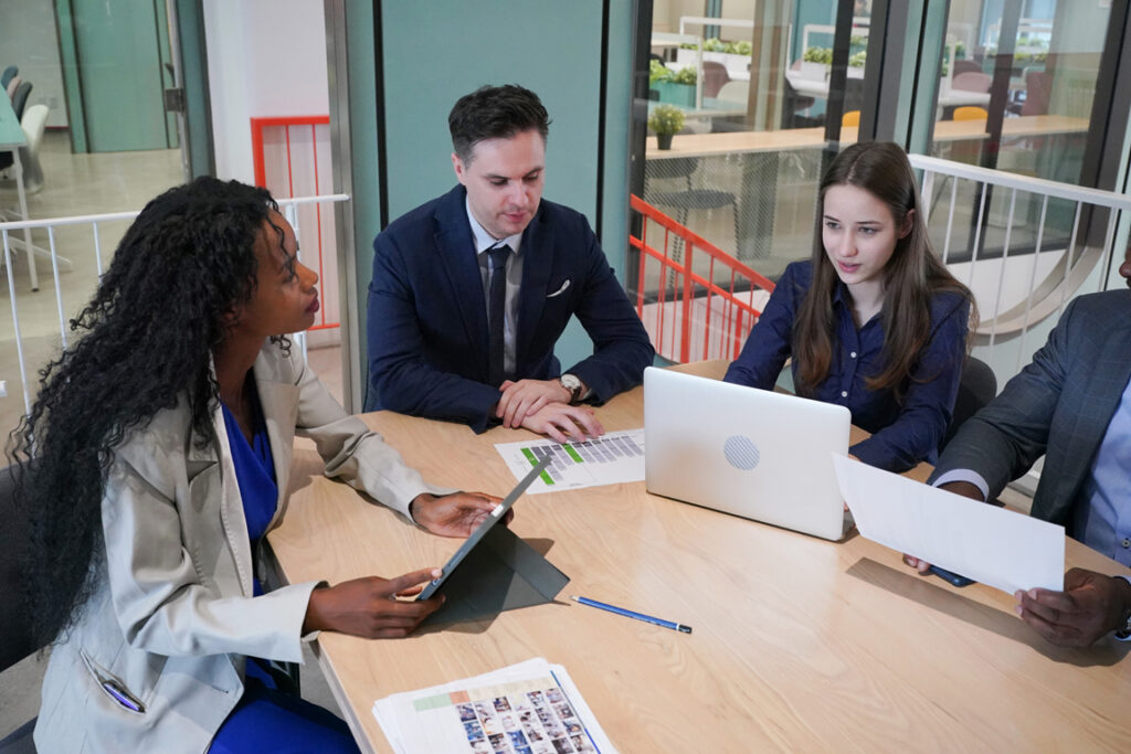 Image of young businessmen and colleague discussing document in laptop and touchpad at meeting
