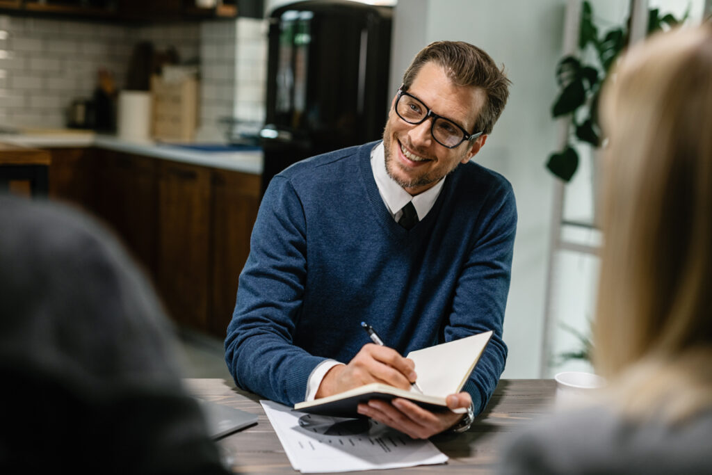 Happy financial advisor communicating with a couple and taking notes into his notebook.