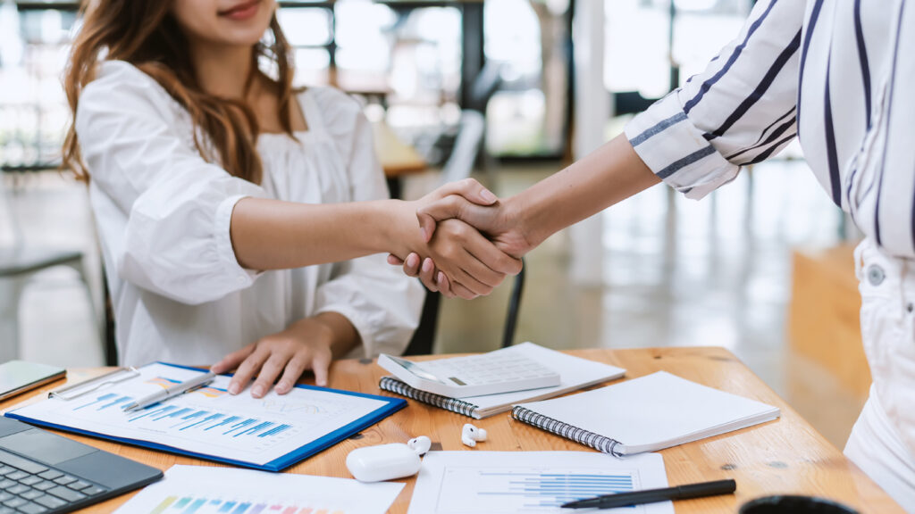 Image of businesswoman shaking hands to congratulate success with graph document Keyboard calculator placed at the office desk.