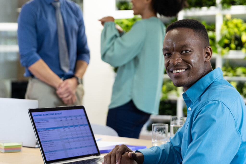 Portrait of happy african american businessman with laptop and diverse colleagues in modern office. Global business, finances and office concept